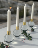 En bild på fyra kristallklot som adventsljusstakar, graverade och målade för hand, där första adventsljuset är tänt lingonris i förgrunden. 