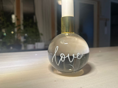 A clear crystal candle holder with 'love' written on it, featuring a gold-colored wick holder at the top, handengraved