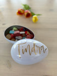 Handmålat vitt påskägg i plåt, fullt med påskgodis. Locket är handmålat med namnet Tindra i guld. 