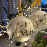 Vit julgranskula i matt färg, med guldfärgat band. Namnet Edith handskrivet på julkulan med guldfärgad penna i modern kalligrafi av Karin Rosenquist-Schager 