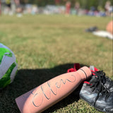 Rosa graverad vattenflaska, fotboll och fotbollsskor i förgrunden. 