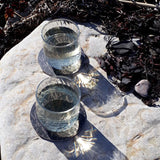 Två glas på svarta underlägg i björkträ, på en sten med svart tång bredvid. 