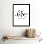 En inramad tavla med texten Fika my favorite f-word på en vit vägg ovanför en hylla. 