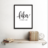 En inramad tavla med texten Fika my favorite f-word på en vit vägg ovanför en hylla. 