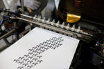 A picture of a book press printing a map of Sweden made from Dala horses in black imprint and gold foiled. 