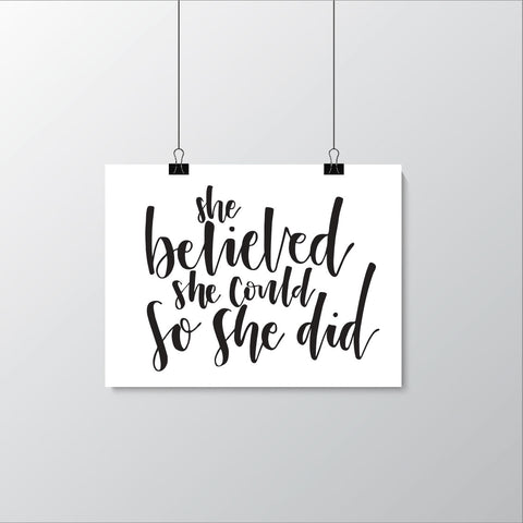 A black and white poster with the text 'She believed she could so she did.' in a handwritten script hanging against a white background.
