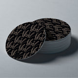 A stack of round glass coasters with a black and white design, featuring the word 'skål' in script, presented on a grey background.